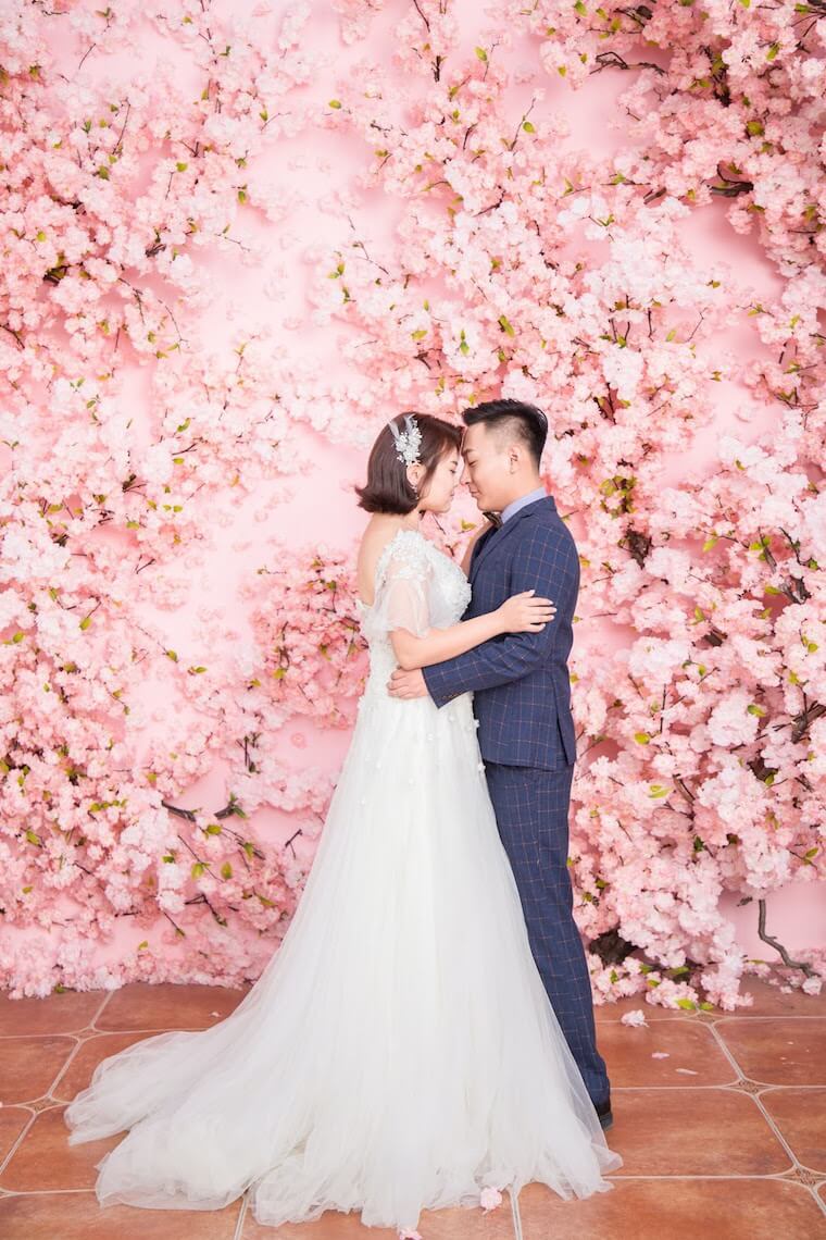 bride and groom in front of pink flower wall 
