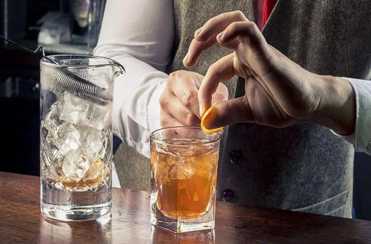 bartender garnishing cocktail with orange peel 