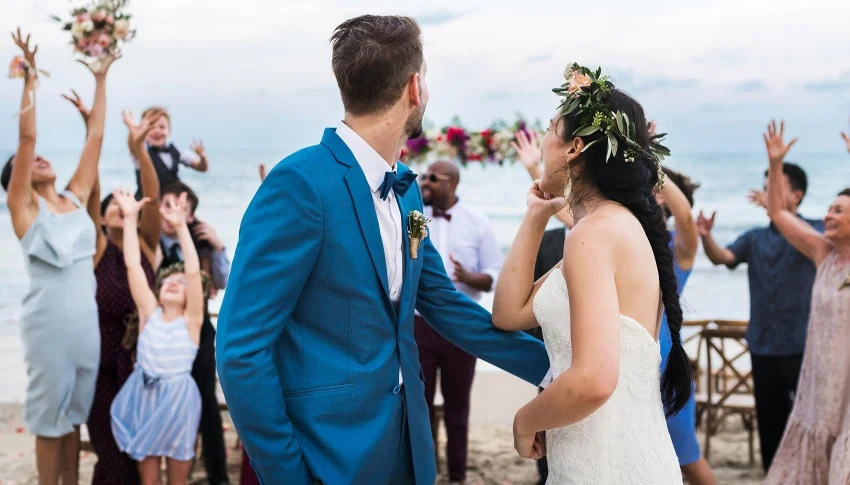 bride and groom on beach throwing the bouquet looking at guests