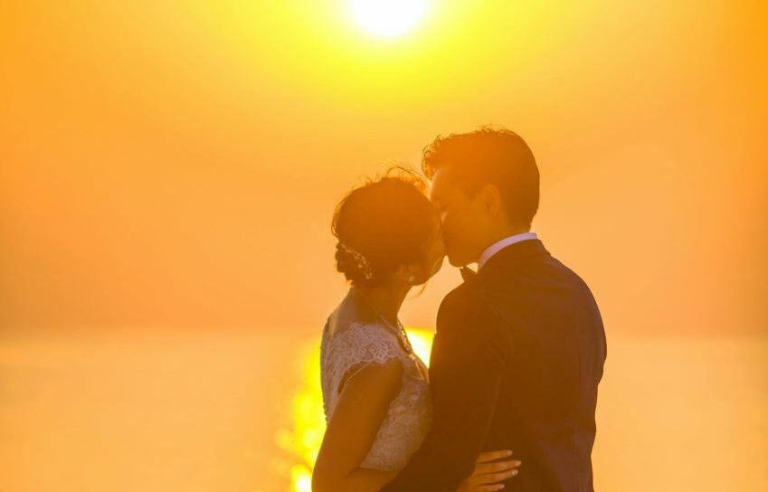 bride and groom kissing during sunset
