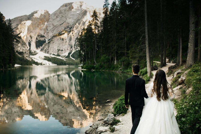 bride and groom walking away from the camera with a mountain and lake in the background