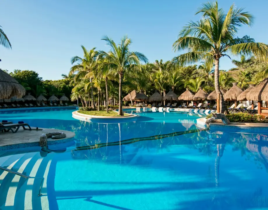 Resort swimming pool surrounded by palm trees and palapas in Costa Rica