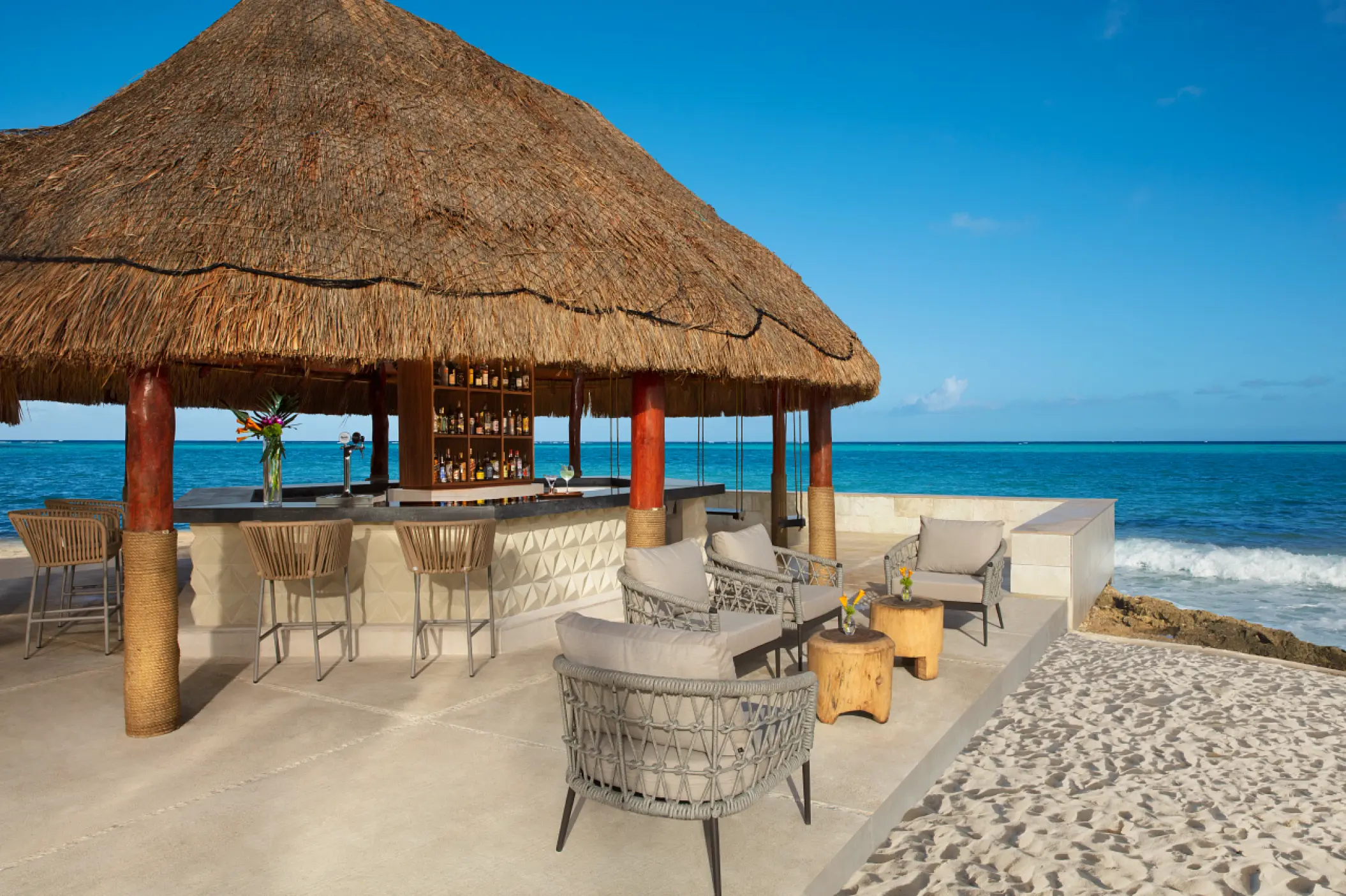 Oceanfront bar with a thatched roof and lounge seating at Dreams Aventuras, Riviera Maya