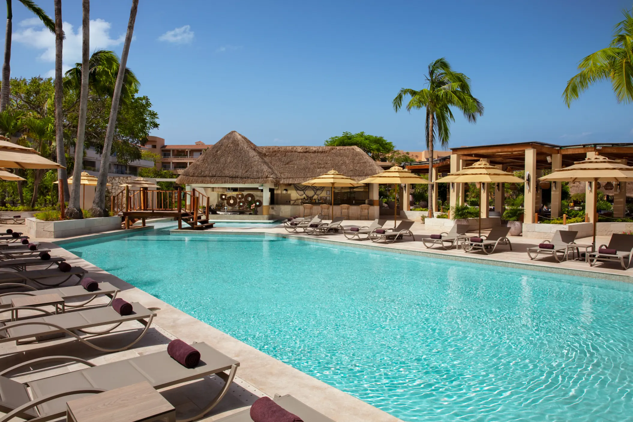 Swimming pool area with lounge chairs and a thatched roof bar at Dreams Aventuras, Riviera Maya