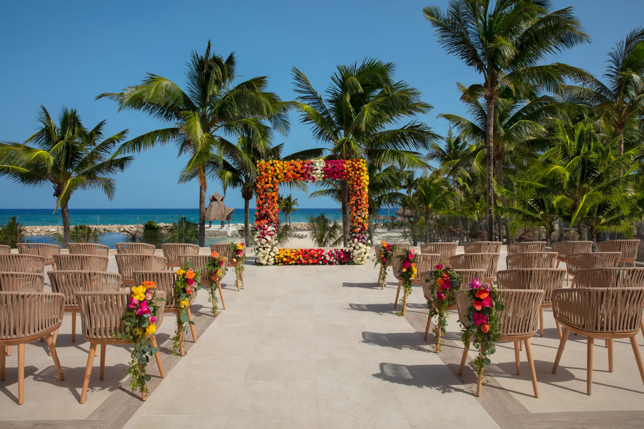 Terrace wedding ceremony at Dreams Aventuras Riviera Maya featuring a vibrant floral arch and ocean views