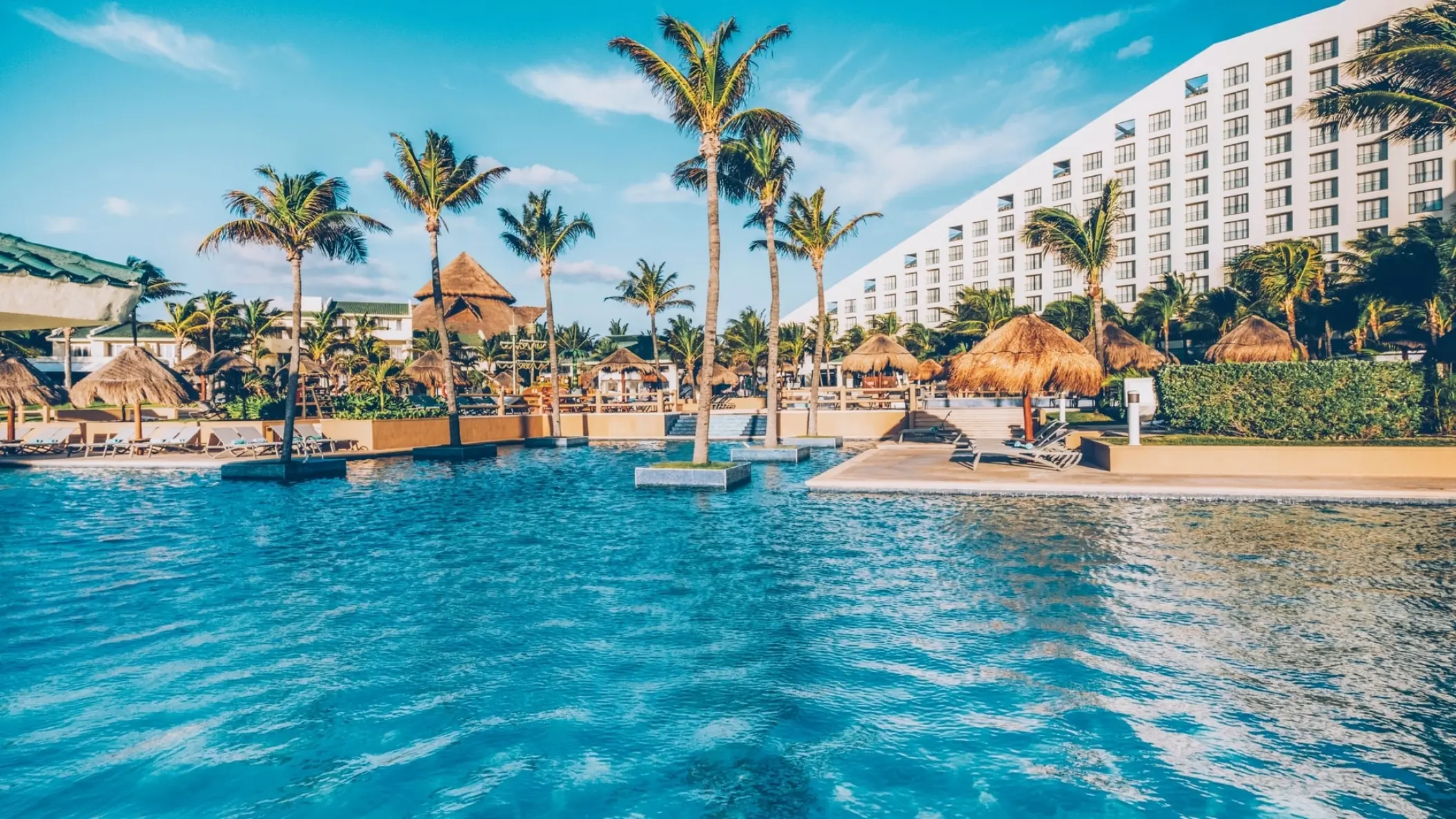 Large swimming pool with palm trees and thatched umbrellas at Iberostar Selection Cancun