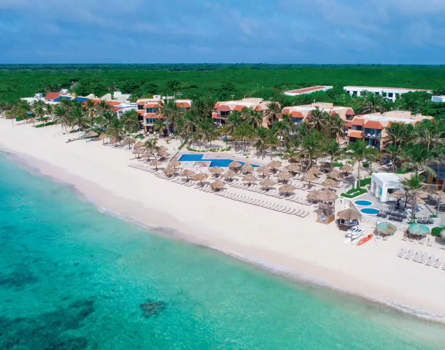 Aerial panoramic view of a beachfront resort with white sand, palm trees, and turquoise water