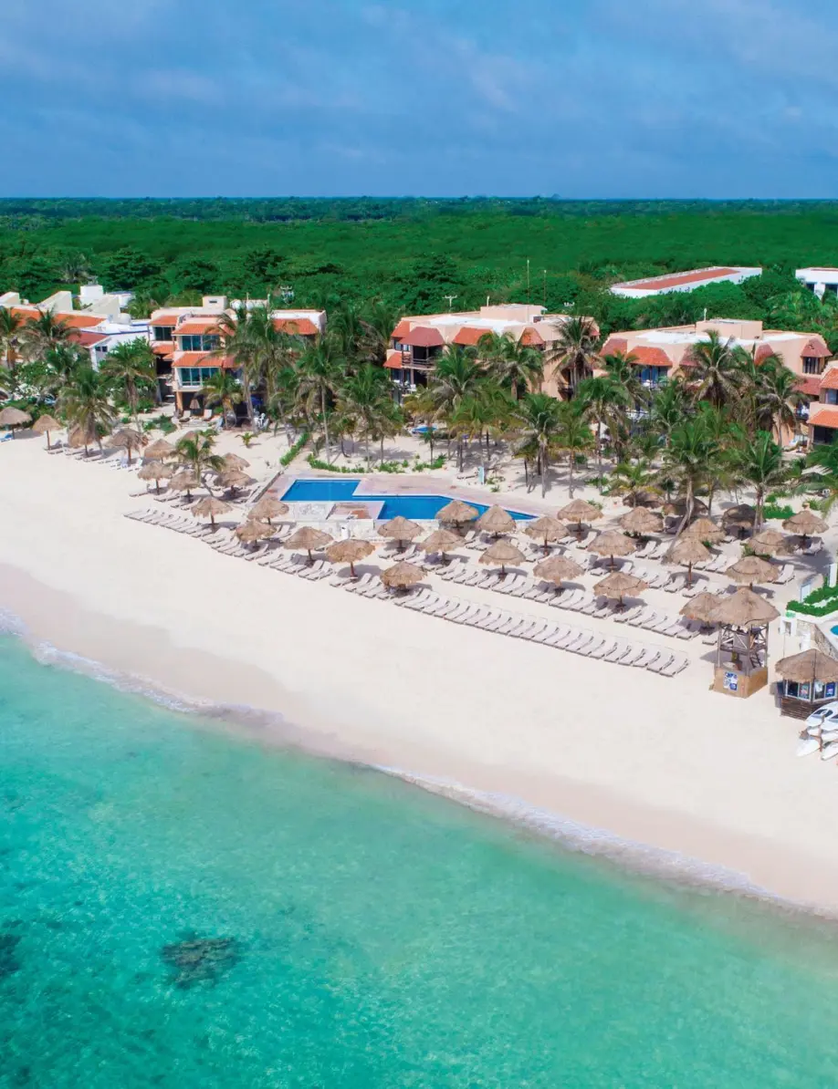 Aerial panoramic view of a beachfront resort with white sand, palm trees, and turquoise water