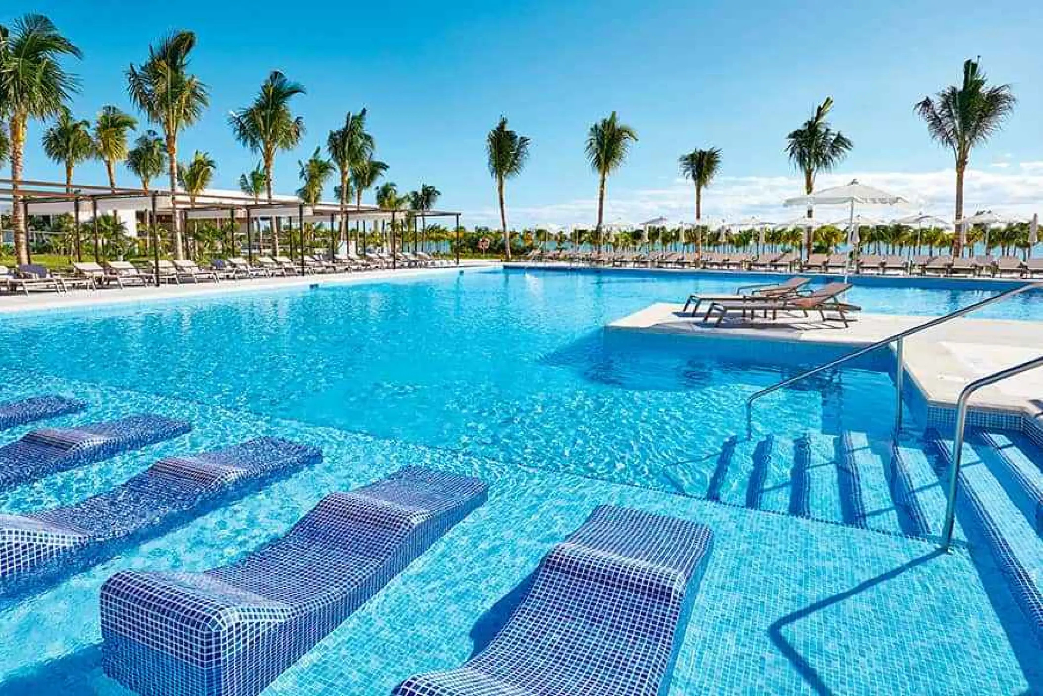 Riu Palace Costa Mujeres swimming pool with submerged lounge chairs and palm trees, Cancun