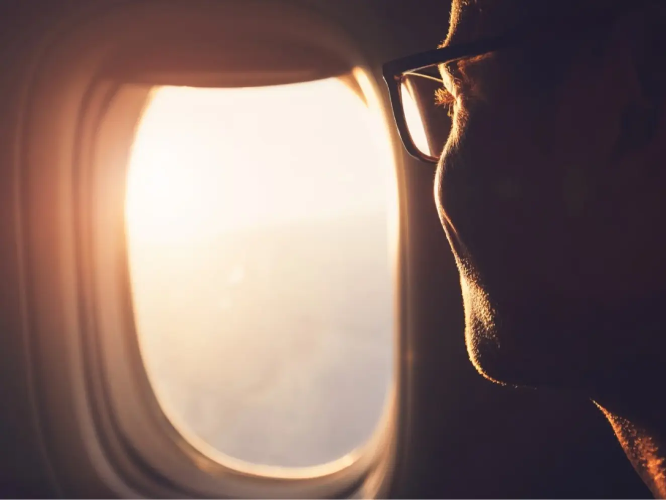Close up of a man looking out of an airplane window at the sunset during a flight to a destination wedding