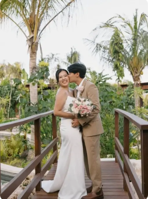 Groom kissing the bride's cheek on a wooden bridge during a destination wedding