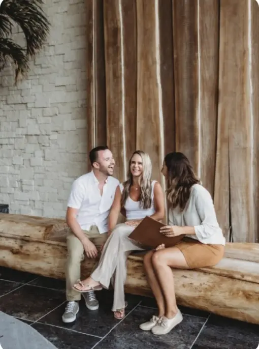 Paradise Weddings planner laughing with a couple on a wooden bench while holding a planning folder