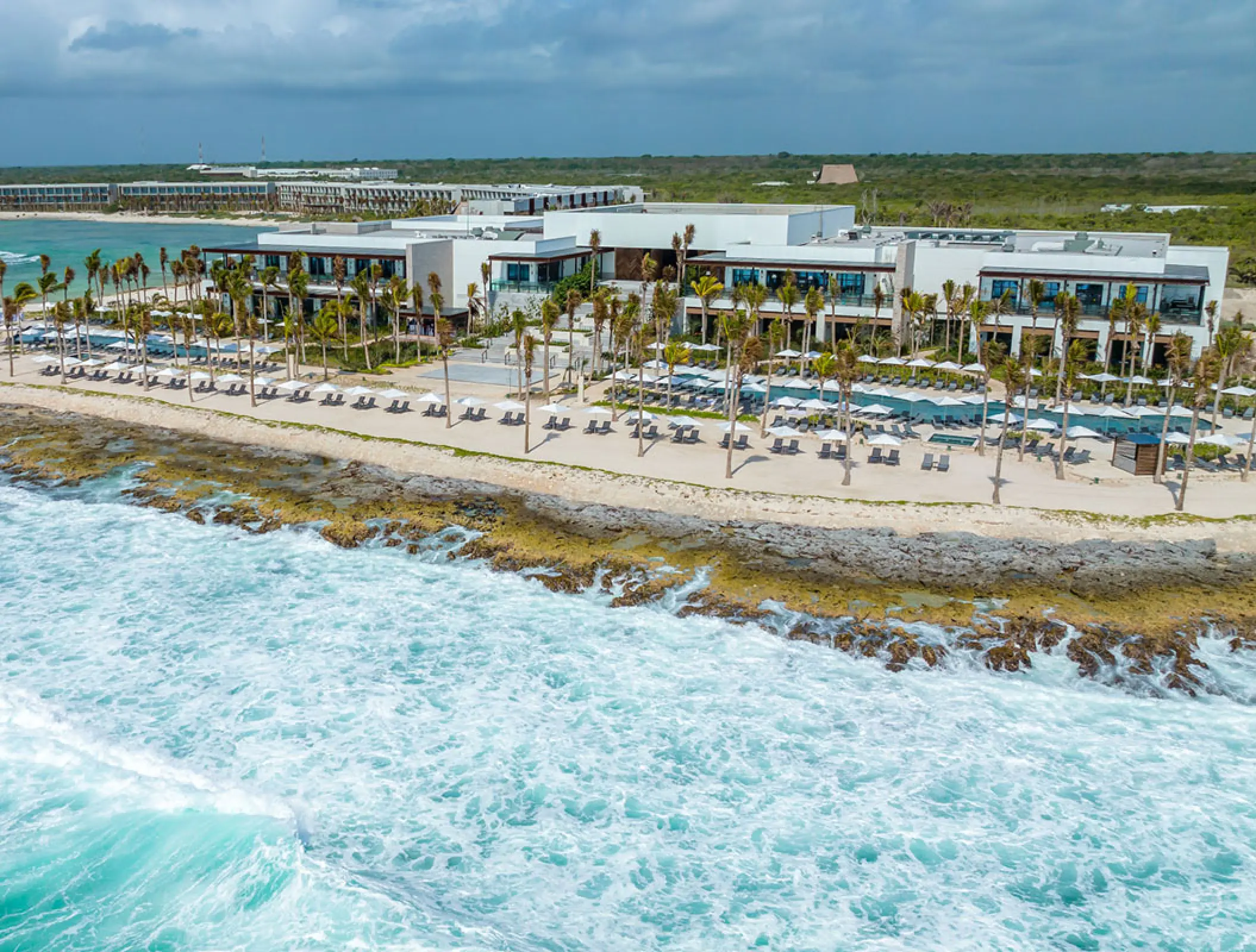 Aerial view of Hilton Tulum beachfront buildings and white sand shore overlooking turquoise waves, Tulum