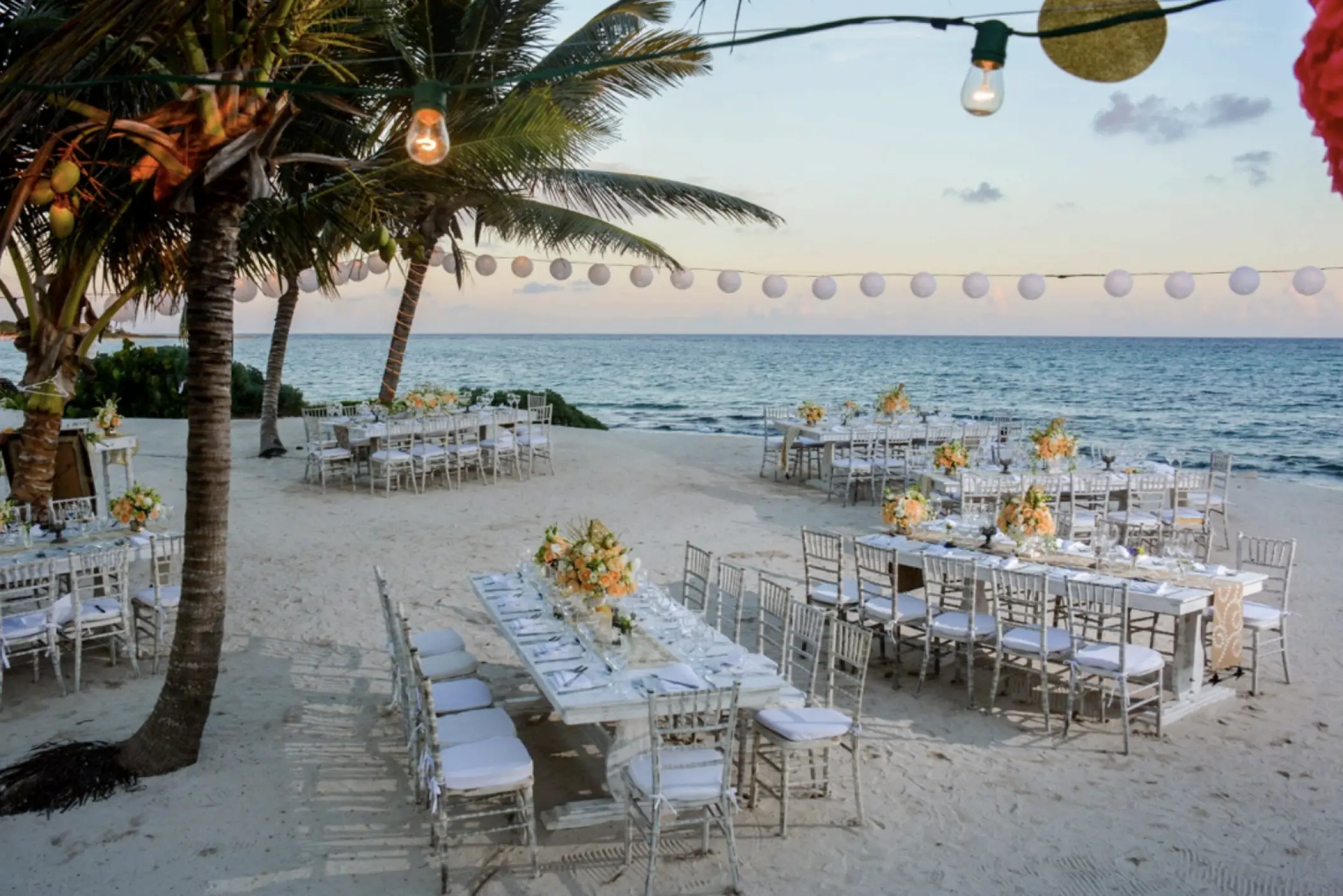 Beachfront wedding reception with long white tables and string lights at Akumal Bay Beach Resort, Riviera Maya