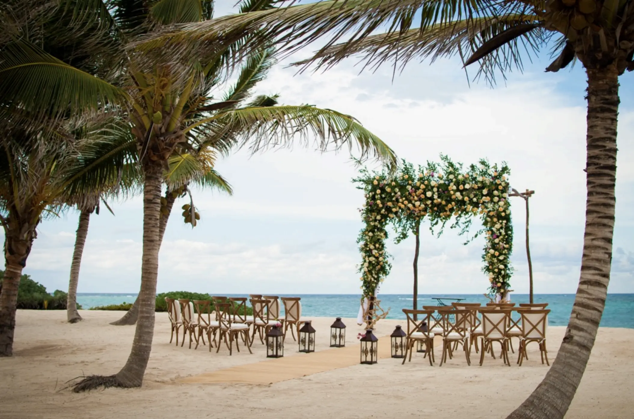 Beachfront wedding ceremony with floral arch and wooden chairs at Akumal Bay Beach, Riviera Maya