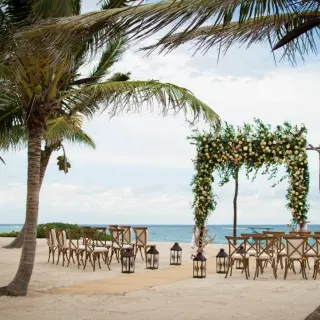 Beachfront wedding ceremony with floral arch and wooden chairs at Akumal Bay Beach, Riviera Maya