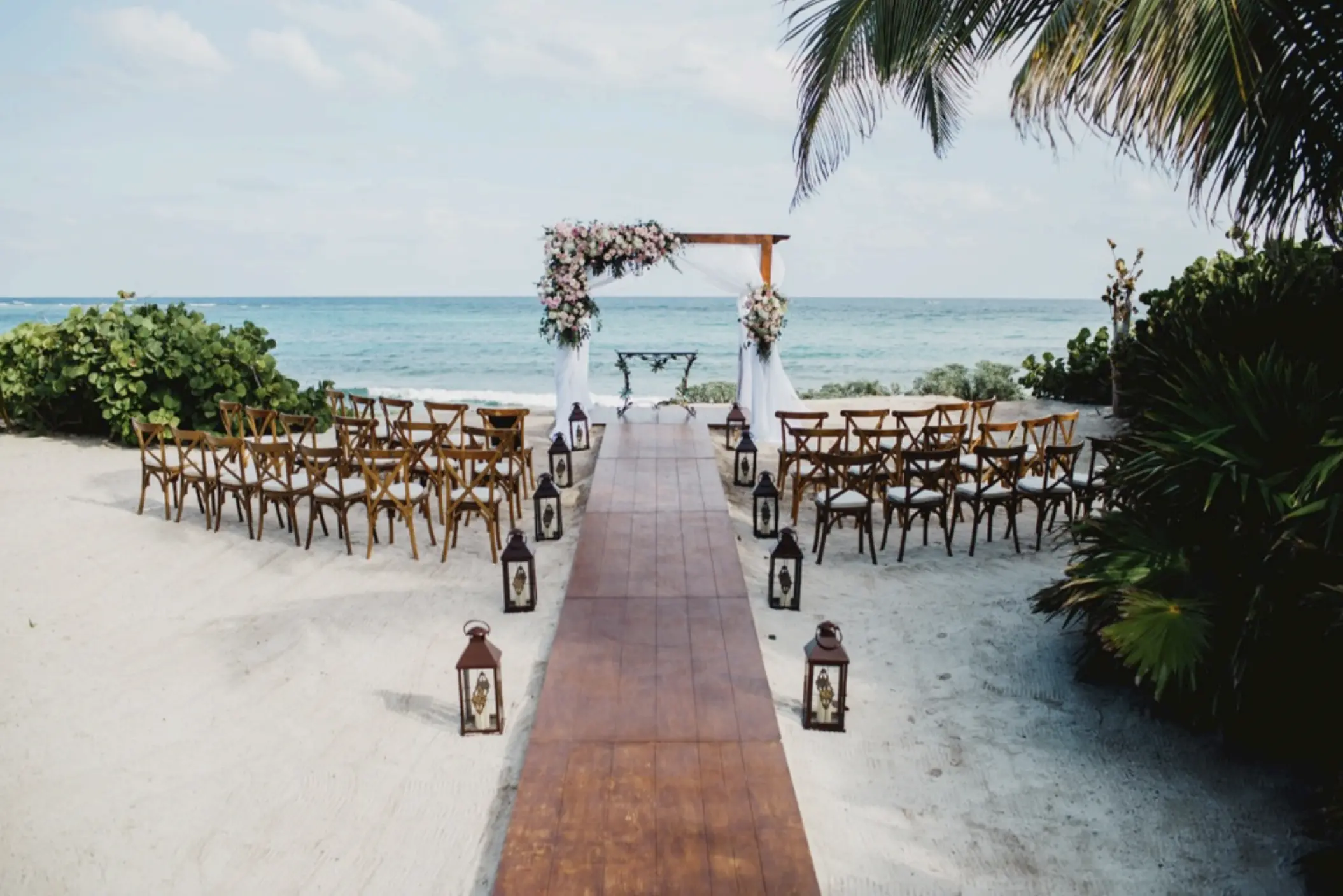 Beachfront wedding ceremony with a wooden walkway and floral arch at Akumal Bay Beach, Riviera Maya