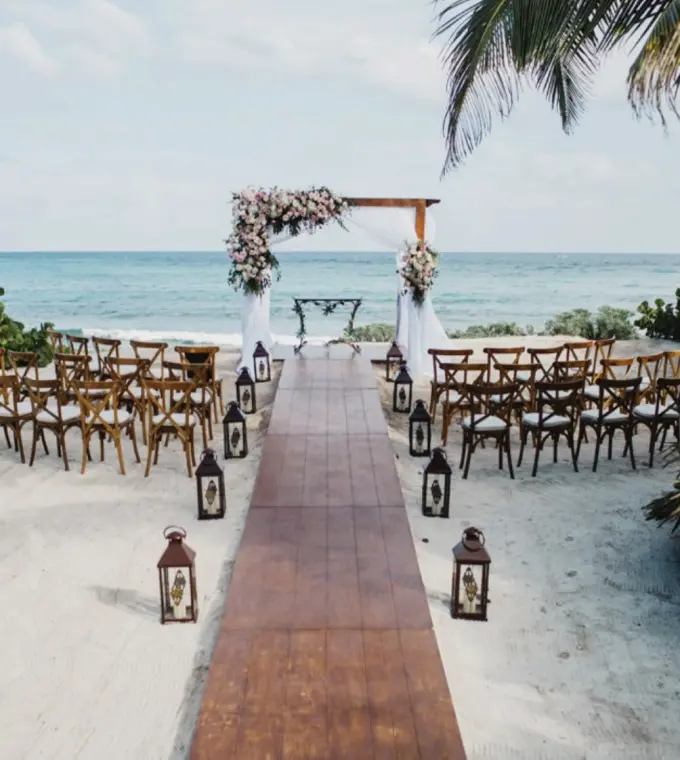 Beachfront wedding ceremony with wooden aisle and floral arch at Akumal Bay Beach, Riviera Maya