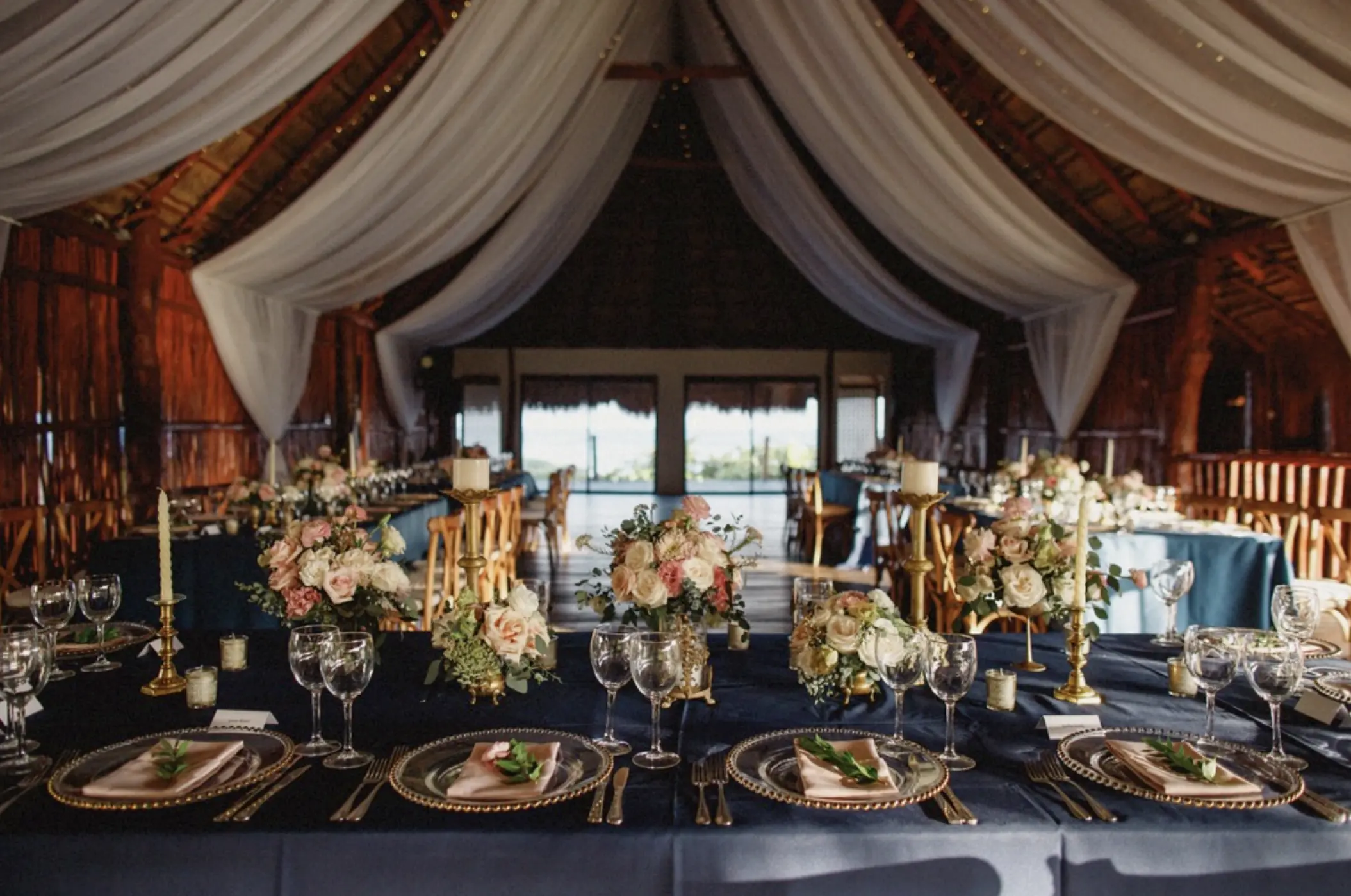 Indoor palapa wedding reception with navy linens and white draping at Akumal Bay Beach & Wellness Resort, Riviera Maya