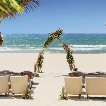 Beachfront wedding ceremony setup with floral teepee arch and lounge seating at Allegro Playacar, Playa Del Carmen