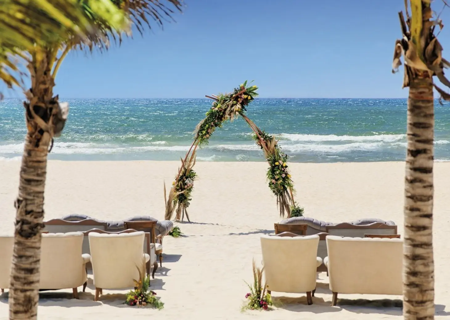 Beachfront wedding ceremony setup with floral teepee arch and lounge seating at Allegro Playacar, Playa Del Carmen