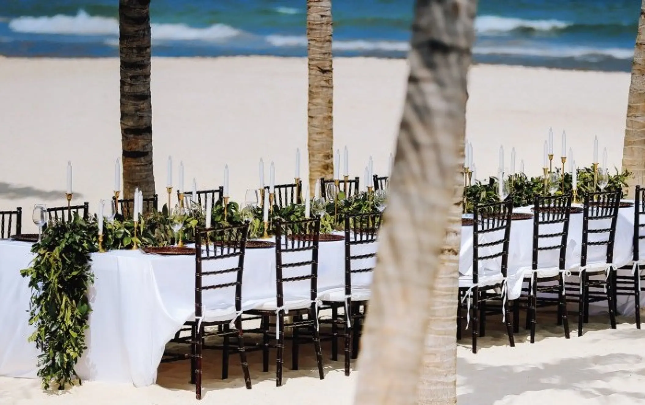 Beachfront wedding reception table with greenery and white candles at Allegro Playacar, Playa Del Carmen