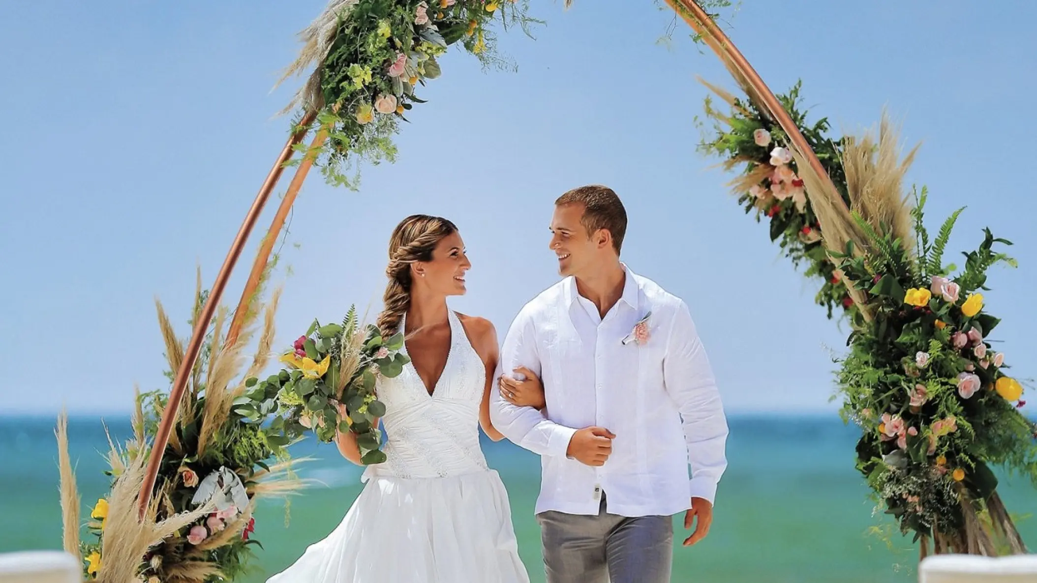 Bride and groom walking under a floral circular arch at Allegro Playacar, Playa Del Carmen