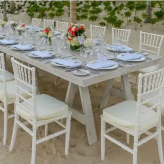 Long white wooden reception table with floral centerpieces on the beach at Atelier Playa Mujeres, Cancun