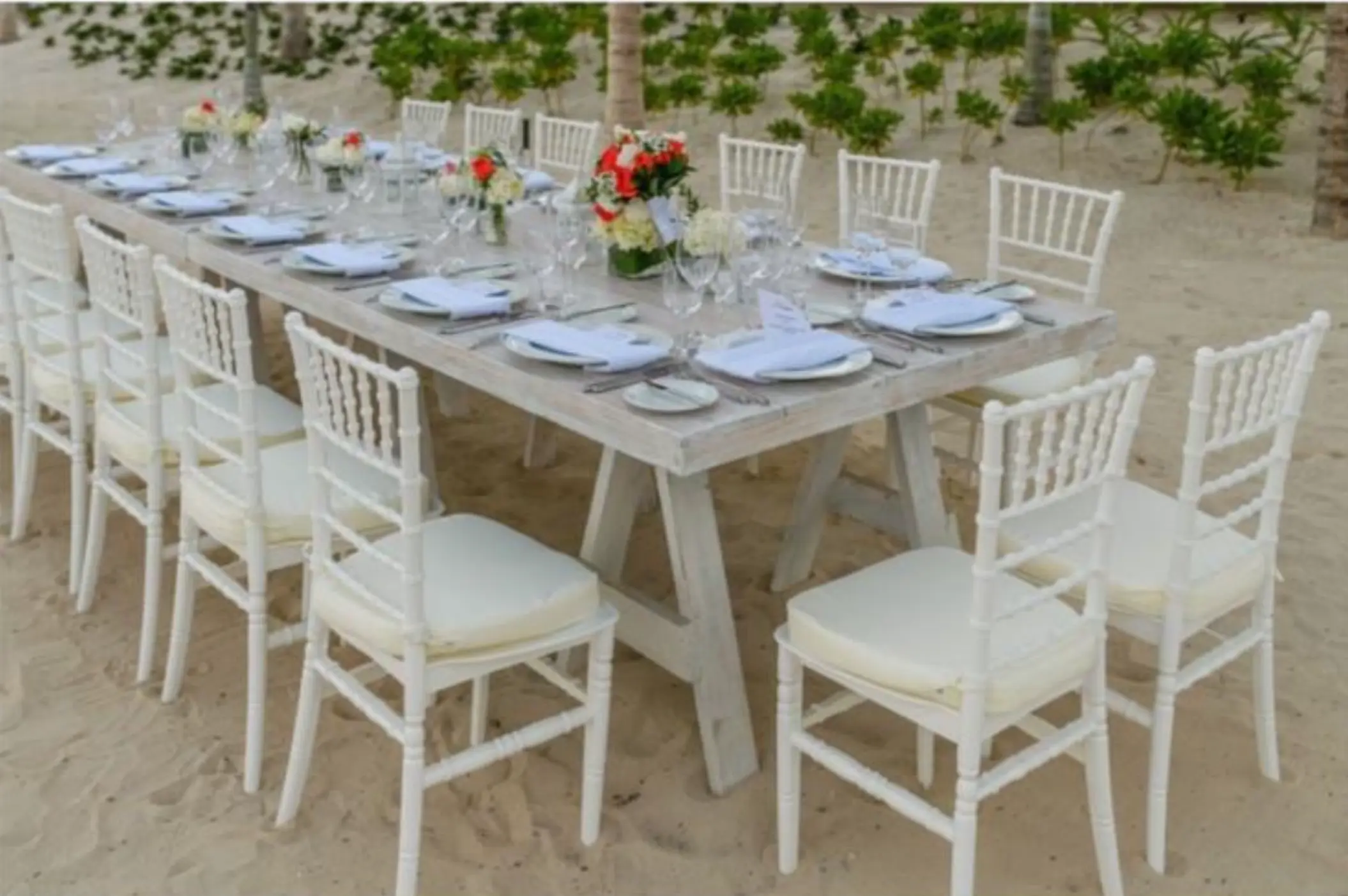 Long white wooden reception table with floral centerpieces on the beach at Atelier Playa Mujeres, Cancun