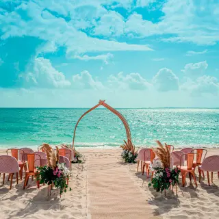 Beachfront wedding ceremony setup with a floral arch and pink chairs at Atelier Playa Mujeres, Cancun