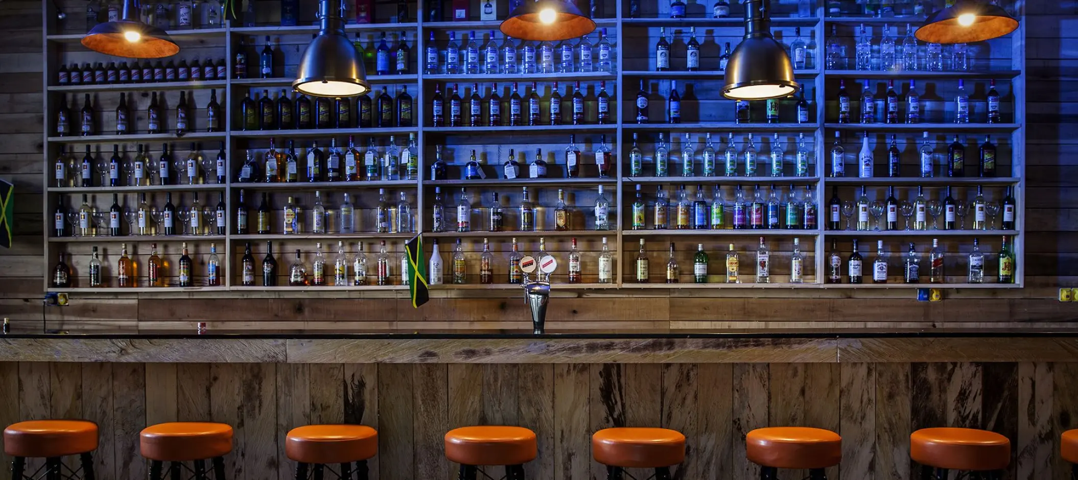 Sports bar interior with a wall of liquor bottles and orange stools at Azul Beach Resort Negril