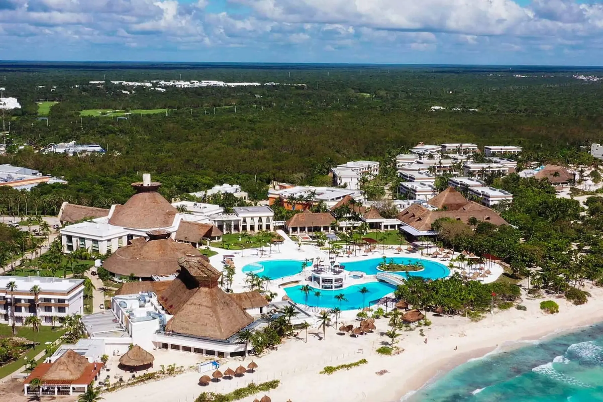 Aerial view of Bahia Principe Grand Tulum pools and beachfront buildings surrounded by lush jungle, Tulum