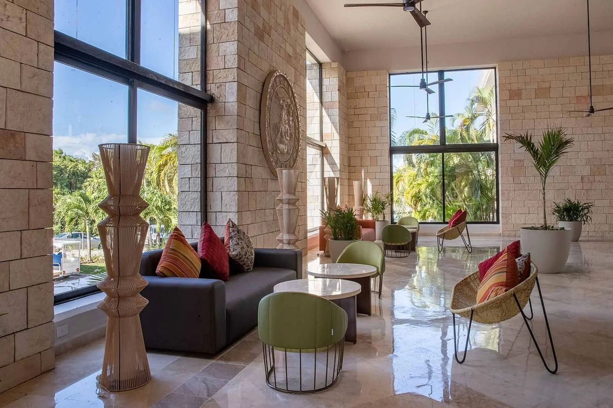 Modern lobby seating area with stone walls and floor-to-ceiling windows at Bahia Principe Grand Tulum