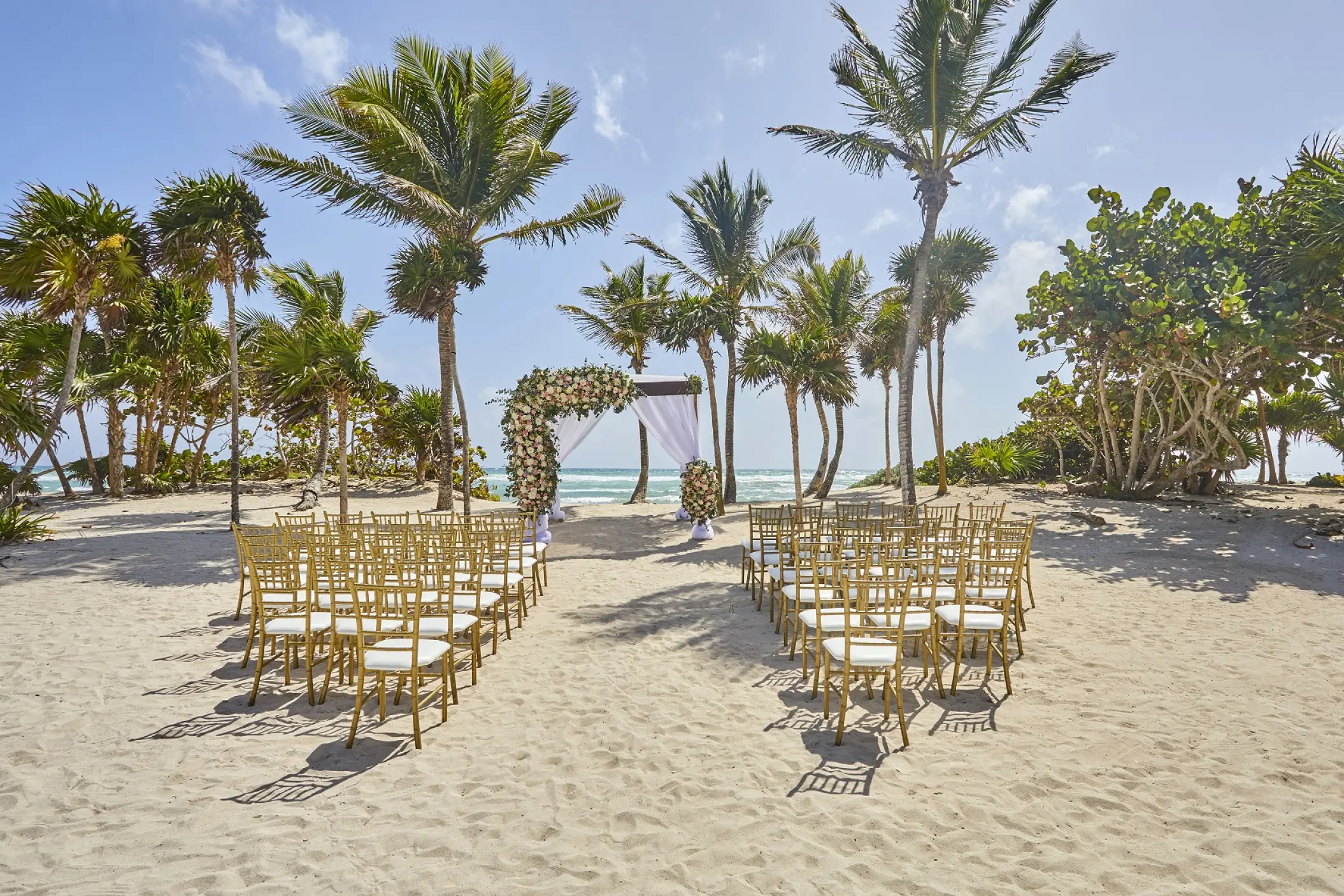 Beachfront wedding ceremony setup with floral arch and gold chairs at Bahia Principe Grand Tulum, Tulum