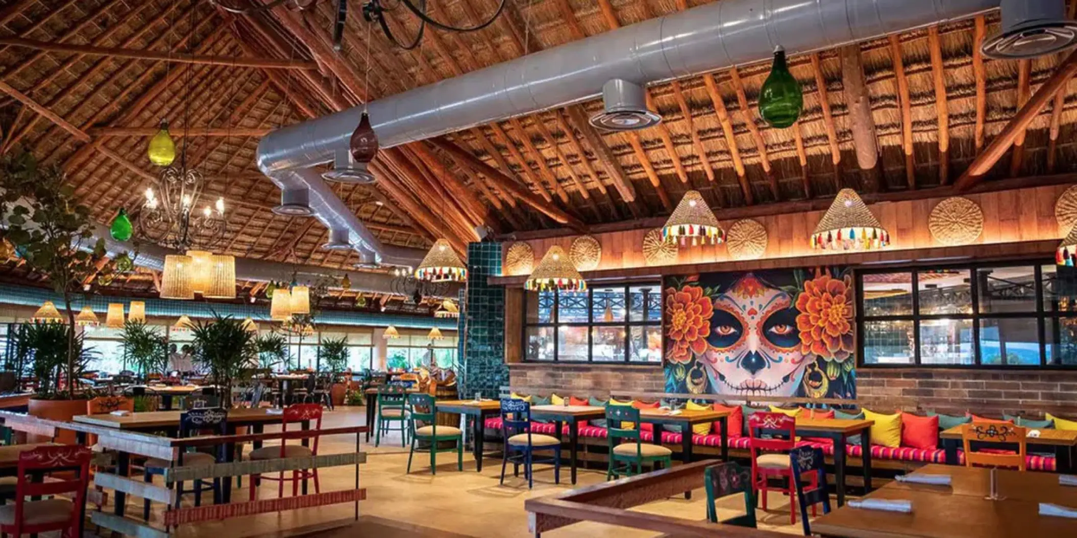 Colorful restaurant dining area with skull mural and thatched ceiling at Bahia Principe Grand Tulum