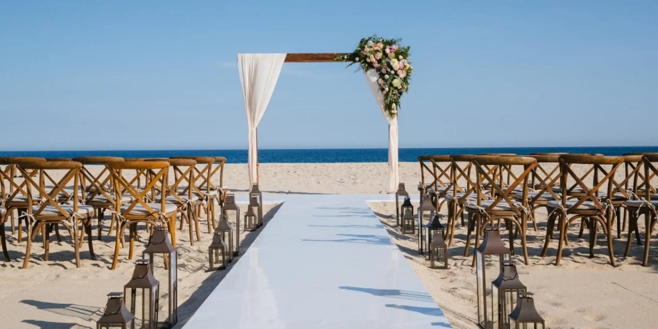 Beachfront wedding ceremony with wooden arch and cross-back chairs at Barcelo Gran Faro, Cabo San Lucas