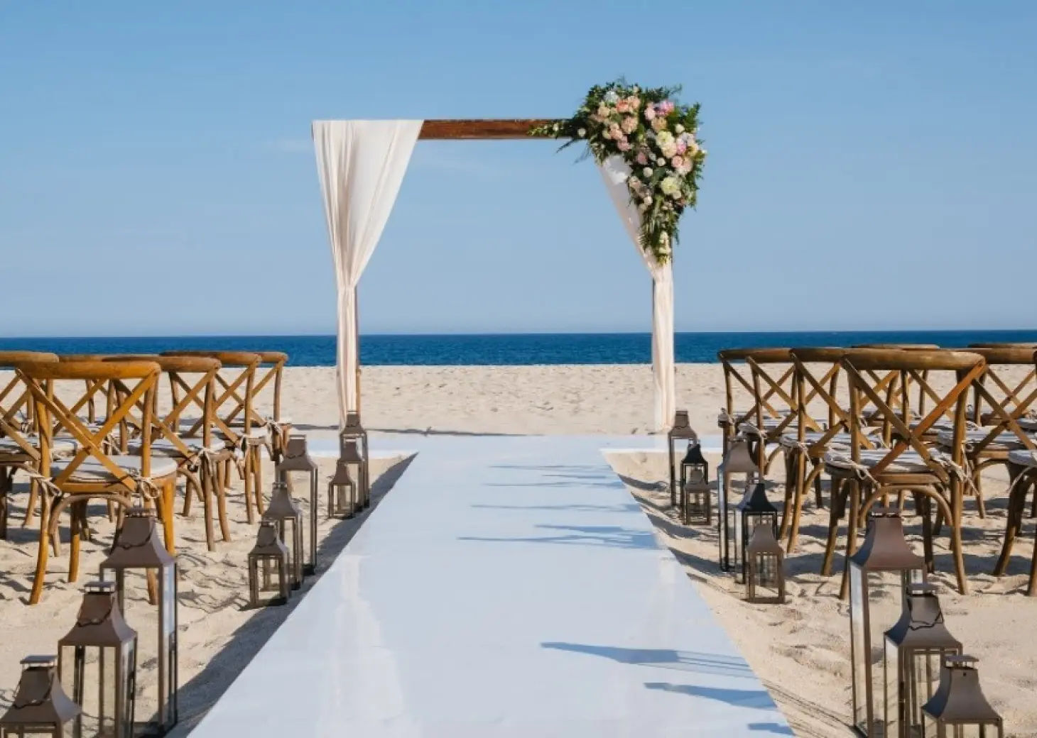 Beachfront wedding ceremony with wooden arch and cross-back chairs at Barcelo Gran Faro, Cabo San Lucas