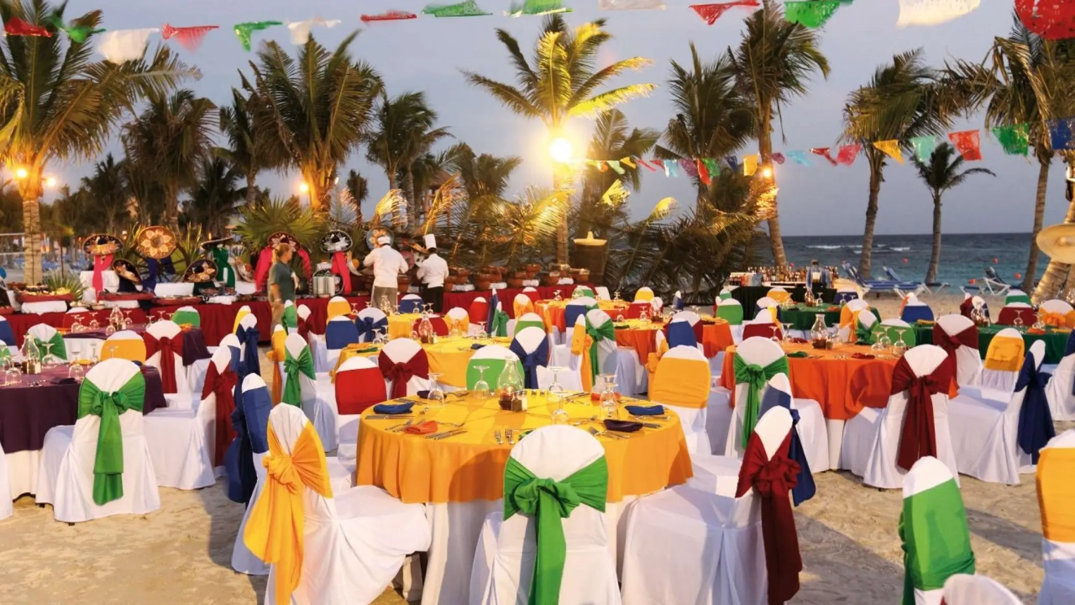 Colorful beachfront wedding reception with papel picado banners and palm trees at Barcelo Maya Caribe, Riviera Maya
