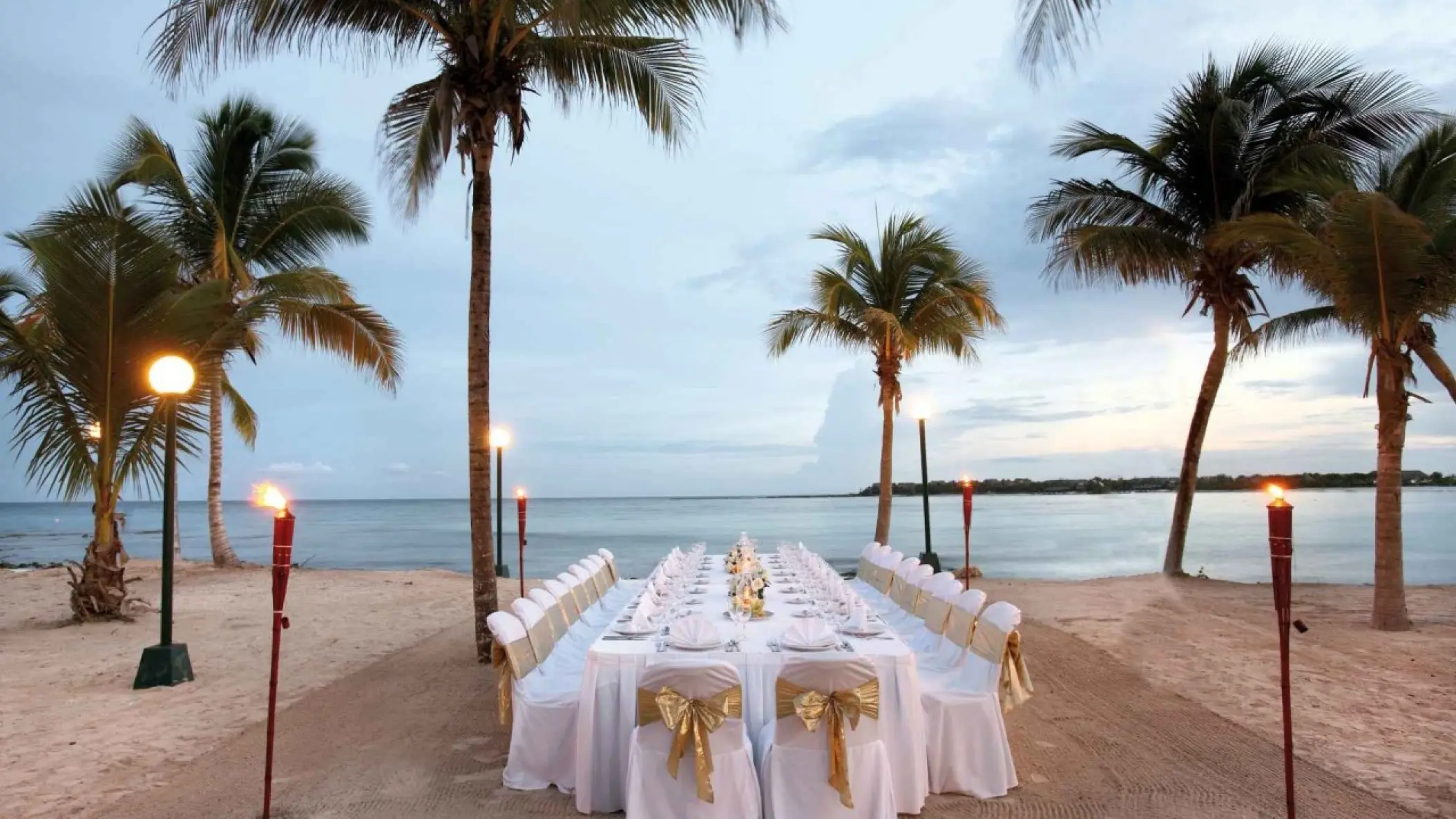 Beachfront wedding reception setup with tiki torches at Barcelo Maya Riviera, Riviera Maya