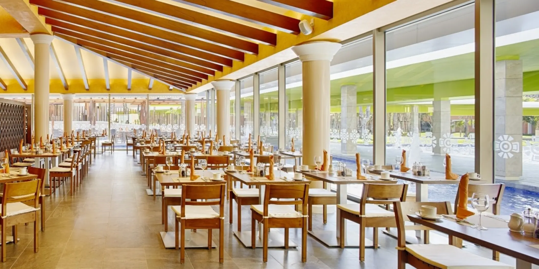 Modern buffet restaurant with wood beam ceilings and floor-to-ceiling windows at Barcelo Maya Beach, Riviera Maya