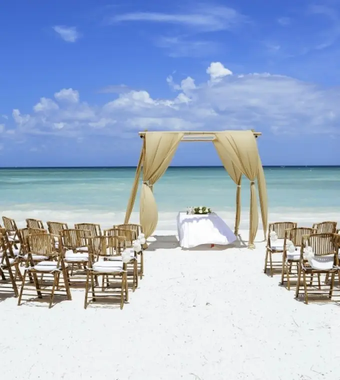 Beachfront wedding ceremony with a draped wooden arch at Barcelo Maya Riviera, Riviera Maya