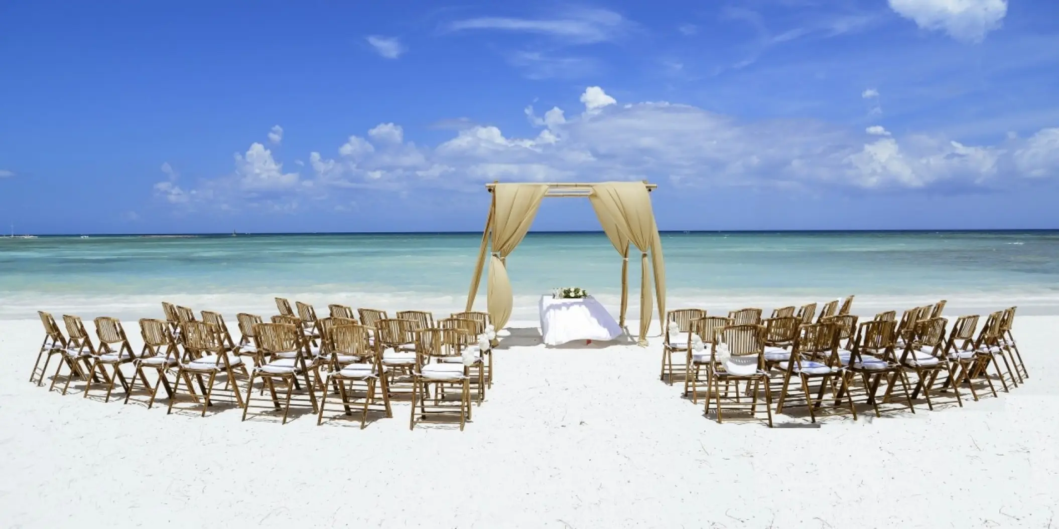 Beachfront wedding ceremony with a draped wooden arch at Barcelo Maya Riviera, Riviera Maya
