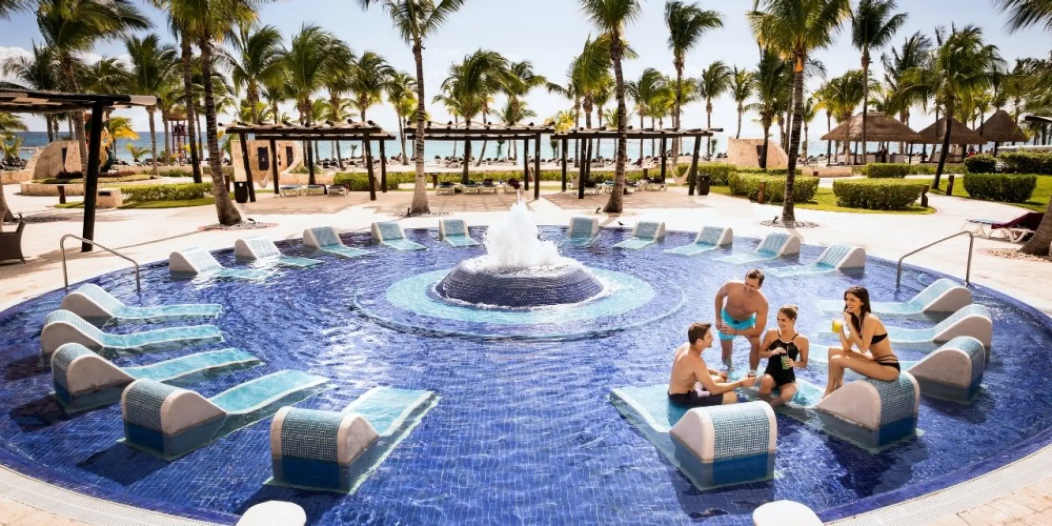 Circular pool with a central fountain and submerged lounge chairs at Barcelo Maya Palace, Riviera Maya