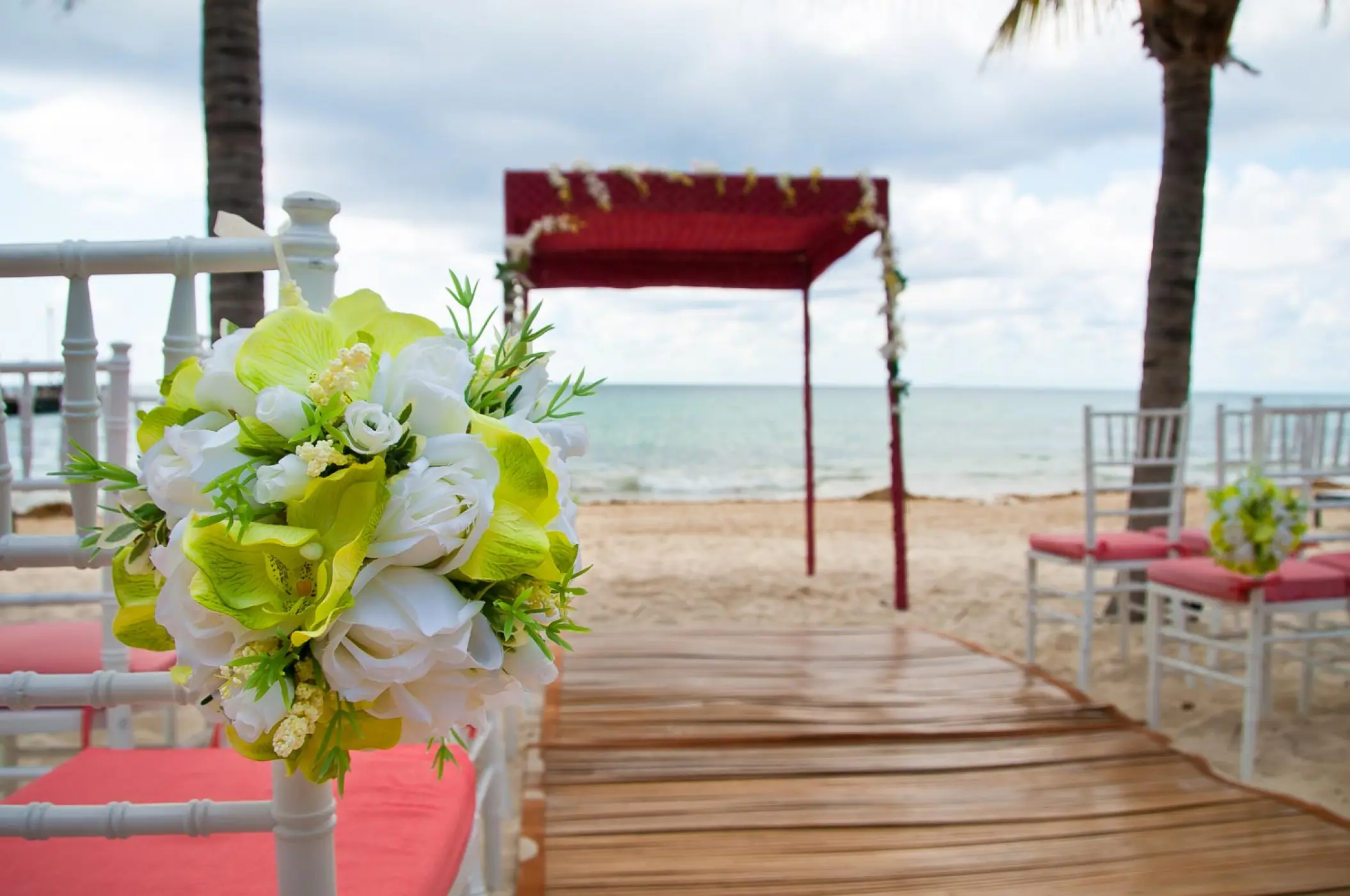 Beachfront wedding ceremony with a red gazebo and floral chair decor at Blue Diamond Luxury, Playa Del Carmen