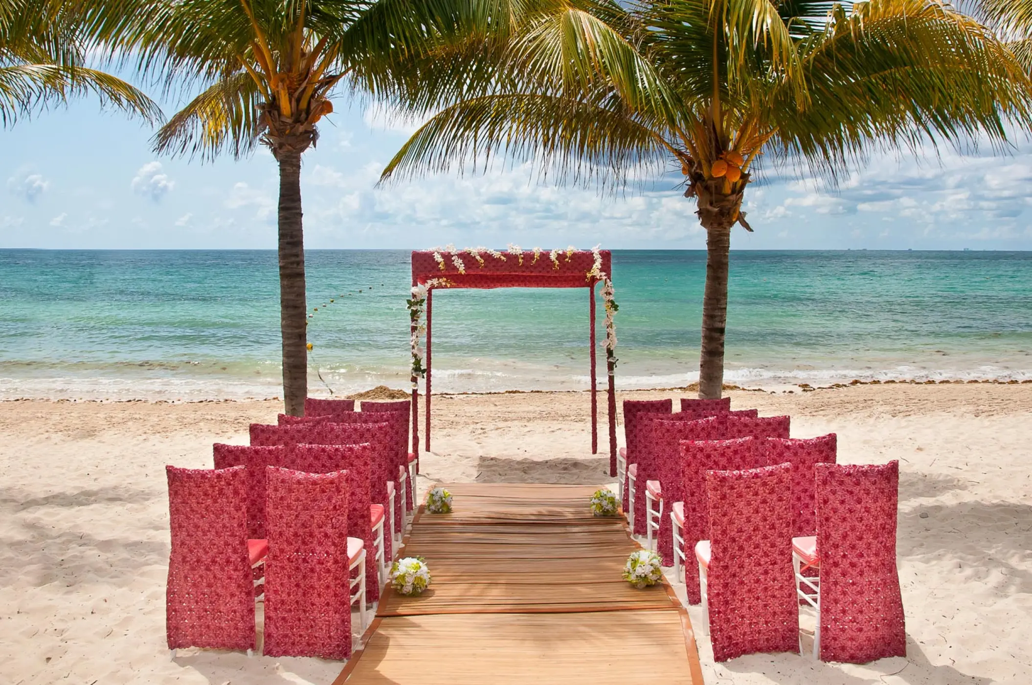 Beachfront wedding ceremony with red chairs and wooden aisle at Blue Diamond Luxury Boutique, Playa Del Carmen