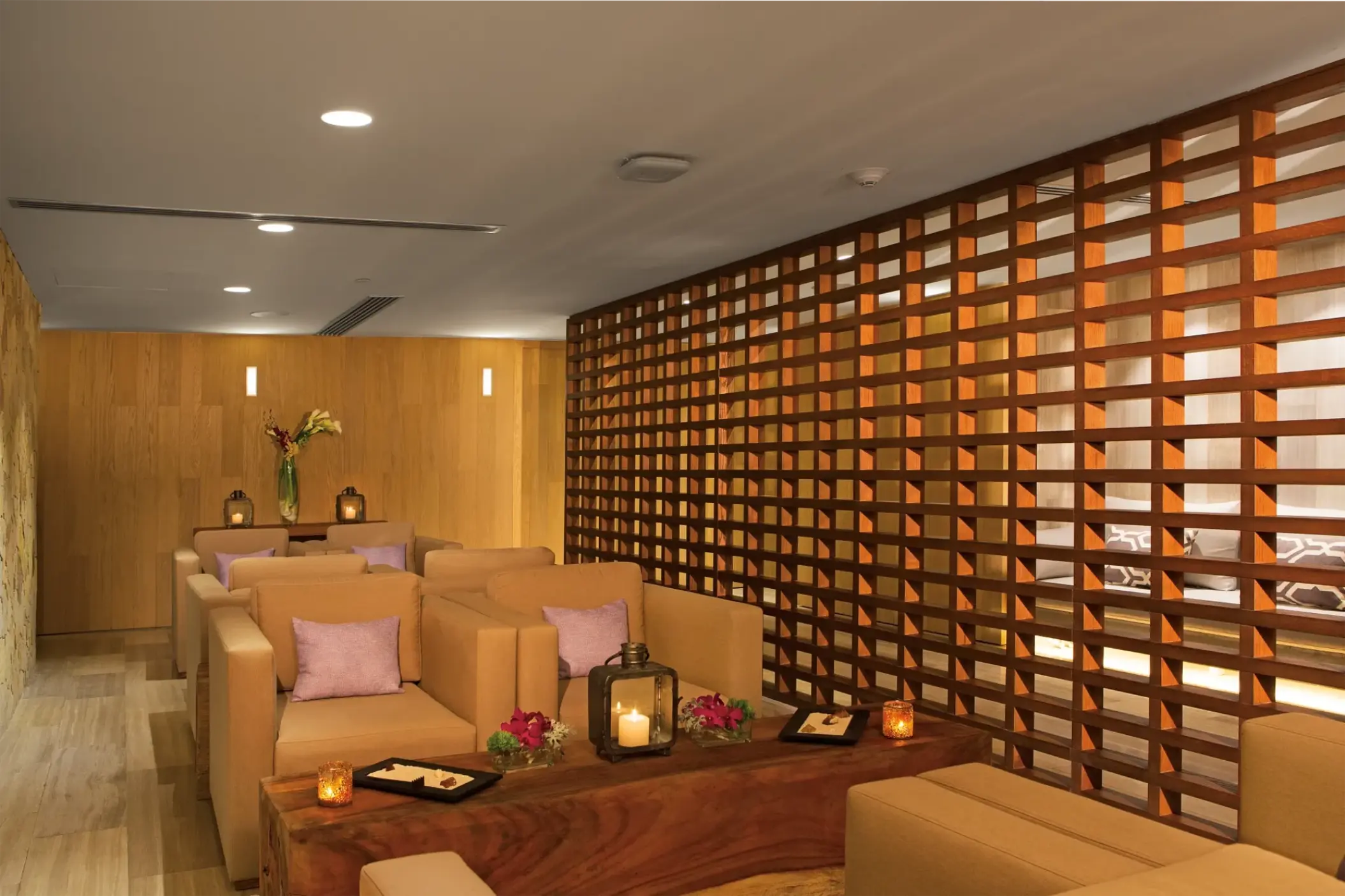 Spa lounge with tan armchairs, wooden lattice wall, and candles at Breathless Cabo San Lucas