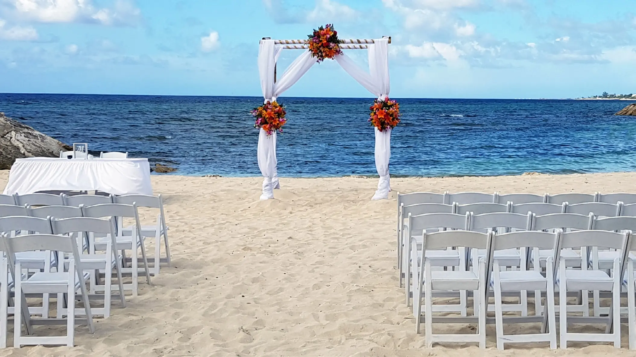 Beachfront wedding ceremony with orange floral arch and white chairs at Breathless Montego Bay, Montego Bay
