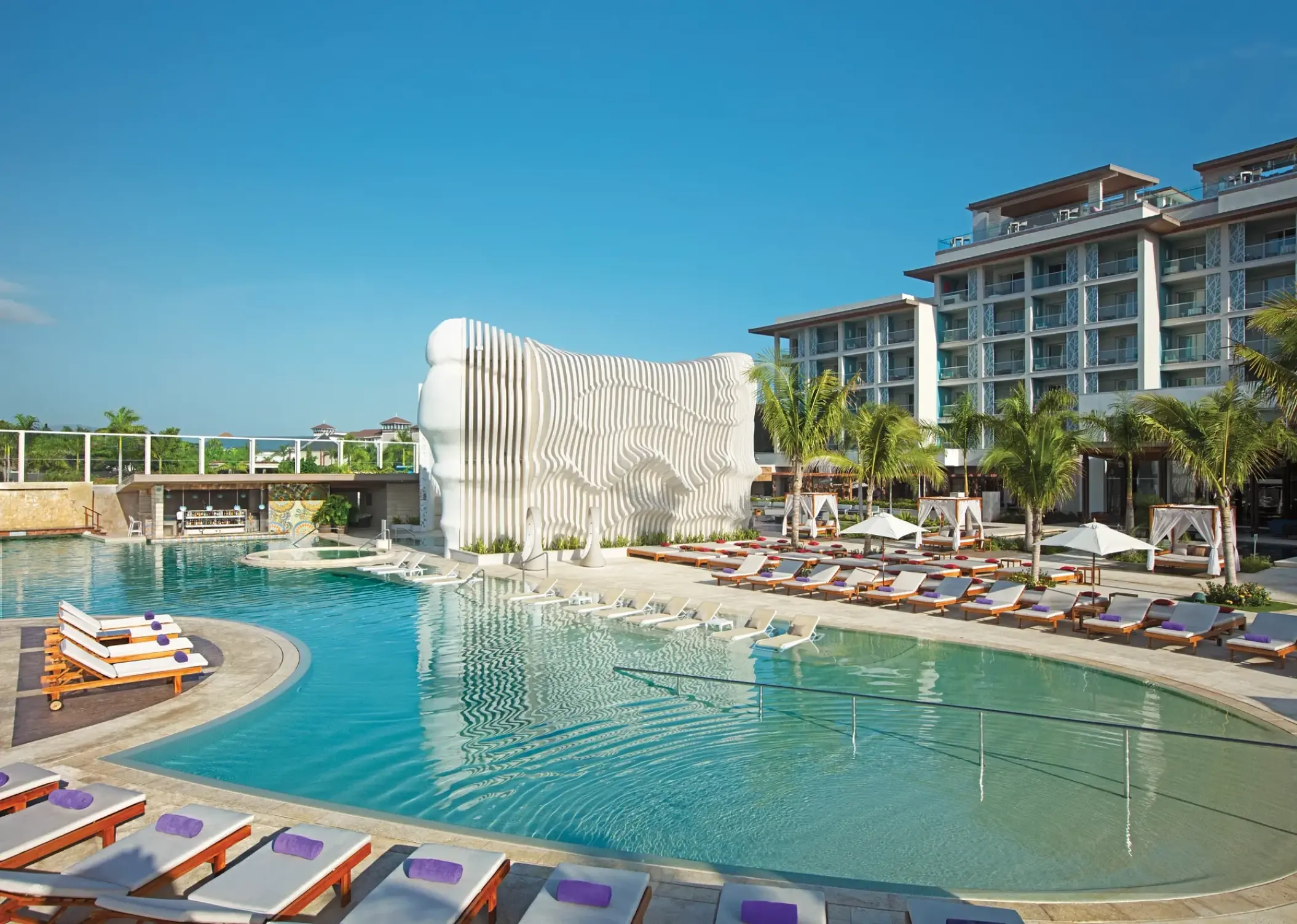 Curved swimming pool with lounge chairs and white modern architecture at Breathless Montego Bay