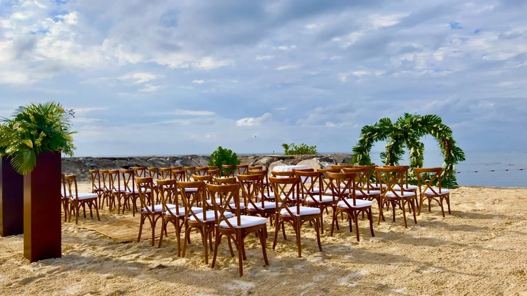 Beachfront wedding ceremony with wooden cross-back chairs and leaf-covered arch at Breathless Montego Bay