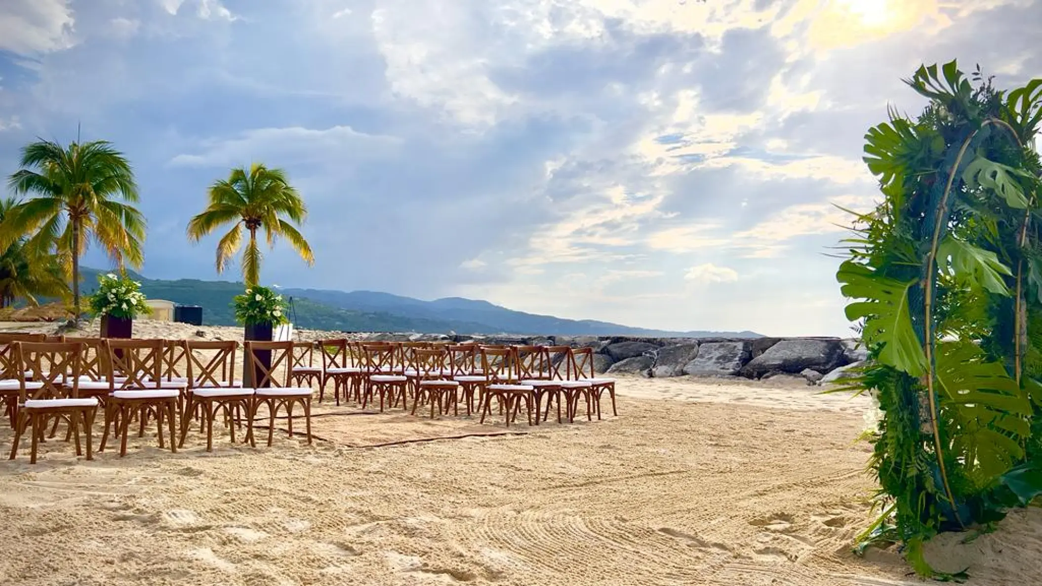 Beachfront wedding ceremony with wooden cross-back chairs and tropical greenery arch at Breathless Montego Bay